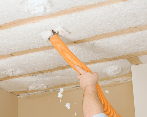 floor-insulation-installation Technician blowing insulation in between floor joists.